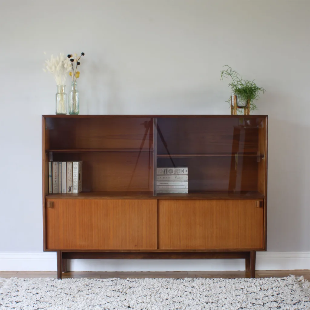 Designed by Robert Heritage for furniture maker, Beaver & Tapley Ltd in the 1960s, this is classic piece of Brit midcentury design. You can see the Scandinavian 'form and function' influence with its sleek, clean lines, but these are partnered with more traditional design elements like the cut of the legs. It's made in teak, teak veneer and possibly a mahogany or dark oak base and legs. We love the pinstripes of grains on the sliding cupboard doors. Expertly made, it's robust and sturdy, perfect for the family home and lots of use. If you don't quite have a space for a sideboard or highboard then this cabinet could be the perfect compromise as you get a good width, loads of storage and display space but a shallow depth that won't intrude into the room.

&nbsp;
