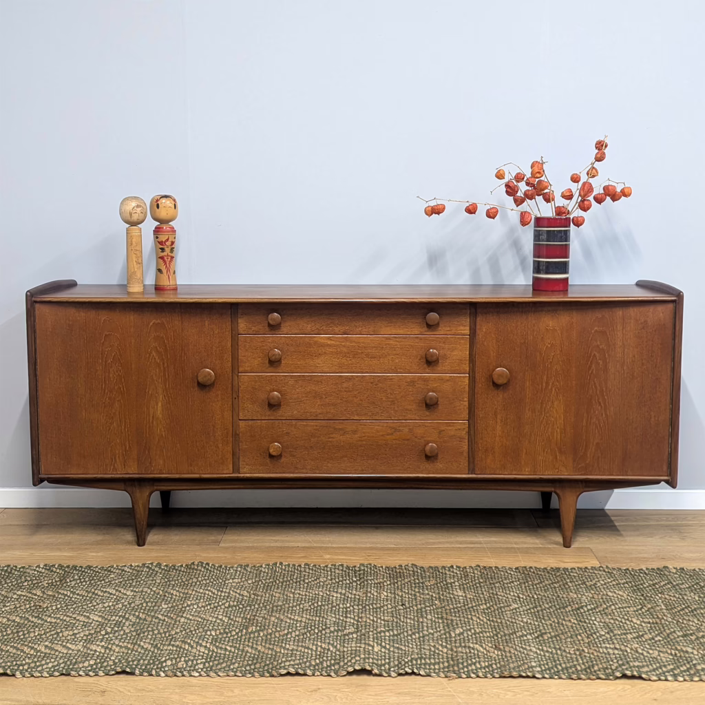 A very fine, British, vintage sideboard designed by John Herbert as part of his Volnay range for A Younger in the 1960s, this is the larger of the two sideboard designs he created. Made in solid teak and at almost two metres in width, this is a heavyweight (literally!), substantial piece providing you with a great deal of practical storage across cupboards and drawers. And yet, despite this, it has retains an elegance and femininity with curves at the front edge and end panels. We particularly love the rather over-sized, round handles. Although midcentury, its design feels more traditional than many retro sideboards so it would be at home alongside pieces from different eras, in different styles. A super piece of attributed British midcentury design in exceptional order.   Free local delivery / Fast UK delivery / Collection welcome!