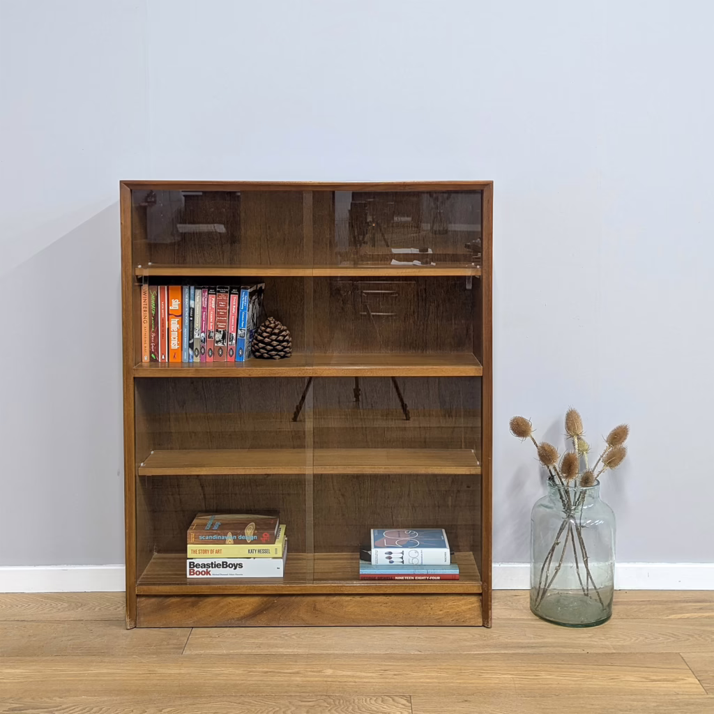 An unfussy, utilitarian vintage bookcase by British maker, Herbert Gibbs, that dates from the early 1970s. Split into two sections, each with its own pair of sliding glass doors and an adjustable shelf inside, it lends itself to be configured to your needs, perhaps with books in one section and treasures in the other. The generous width but shallow depth make this a small footprint storage option where you don't want shelves that intrude into the room too much. It could be put to great use in a child or students' bedroom, or indeed a hallway or landing. Simply designed but very well-made. We have a matching pair of these bookcases available individually and as a set at a discounted price