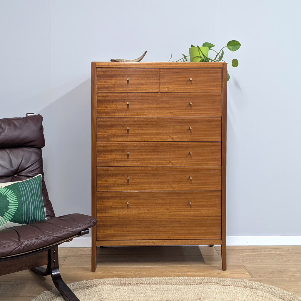 As tallboy dressers go, this one is something special and a rather enigmatic find. We attribute this to Loughborough Furniture, a high-end piece made for Heals of London and it dates from the late fifties / early sixties. Don't be thrown by the Maple name plate inside... it's a red herring! We think this was added at a later date where the rectangular Loughborough Furniture label would be been in the top inside drawer. Our conclusion that it was retailed through Heals fits because this is a piece of the finest quality in terms of construction, wood quality and contemporary design of the time. The richly grained teak stripes across the seven graduated drawer fronts and exterior surfaces. The lower drawer is double height and one of the upper drawers is partially sectioned for accessories. It's one of those pieces that looks of its day and modern at the same time. Elevated on long, elegant legs that flow from the top down to the floor, there is space around an otherwise substantial piece of furniture. We love the discreet brass pull handles too. Tallboys are excellent storage options for rooms where wall space is at a premium. Because they go up rather than along they're a smart use of space, maxing out of height but not compromising on storage. A very fine piece of handsome British midcentury design and one for collectors. This is a keeper.