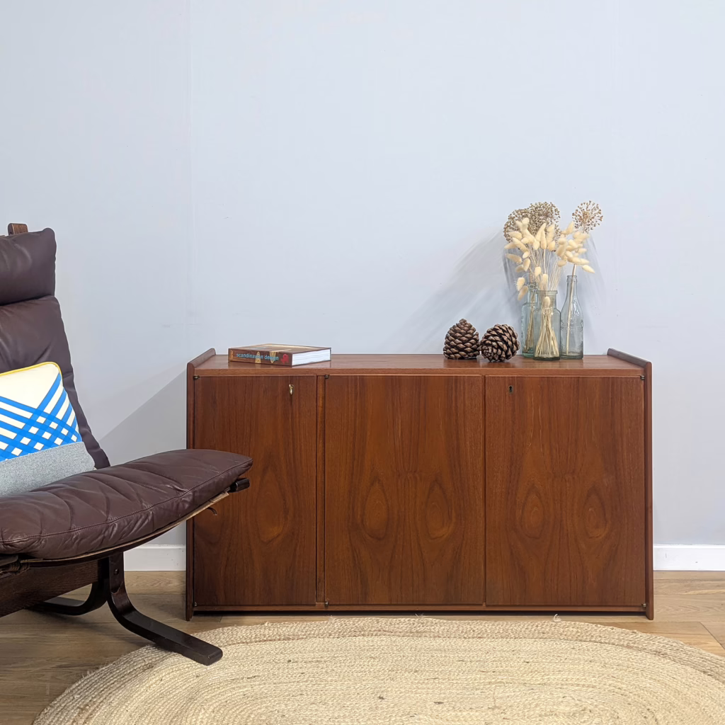 The story goes that this handsome, bespoke Danish cabinet was part of an extensive modular system of wall units, commissioned by a wealthy Brit to have installed in their British home some 50 odd years ago. The cabinets, units, shelves and fittings were made by the same manufacturer who crafted furniture for renowned Danish brand, Drylund, no less. This tells us a great deal about the high quality of this piece, both in terms of design, teak and construction. A great deal of thought, time and money was invested in it. Our supplier was tasked with dismantling the system in recent years but hadn't got round to marketing it so we were delighted to take it off his hands! The design means that the cabinet can sit directly on the floor for use as a sideboard or media stand (it's a good height for a TV on top). The look is about as minimalist as you can get... uninterrupted expanses of warm, richly grained teak. Just marvel at the patina on the door fronts. Inside are adjustable shelves and both cupboards can accommodate vinyl. As you browse through our photos, you'll see the fittings at the back should you wish to use it as intended, mounted on the wall. We're told it simply slotted onto securely moored screws. A one-of-a-kind piece, truly unique and a midcentury original with a great narrative and pedigree.