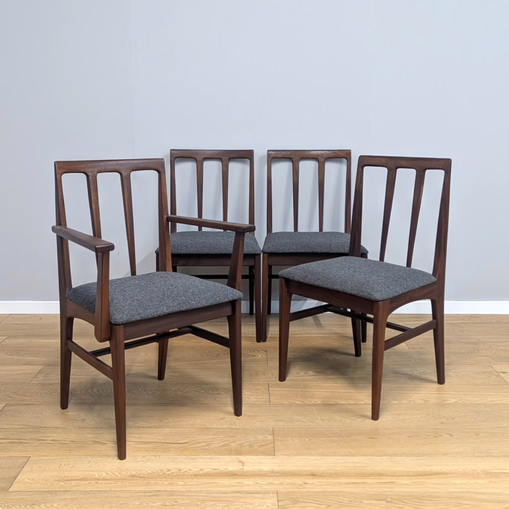 A Younger Ltd was a British midcentury leader throughout the 1950s-1960s, producing low volume, high-end pieces, often retailed through Heals. In collaboration with John Herbert, it was one of the first to be influenced by its Scandinavian contemporaries and that shows in the design of these chairs. Herbert worked with Younger for many years producing several ranges of domestic furniture including his popular 'Volnay' collection which these chairs were part of. Crafted in dark, solid afromosia, these are substantial, supportive chairs, giving much comfort with their contoured backs and generous seat widths. This set includes one carver chair for the head of the table. We have upholstered the seat pads with a smart, charcoal grey, marl pure wool, a sophisticated, contemporary look for these fine midcentury chairs.