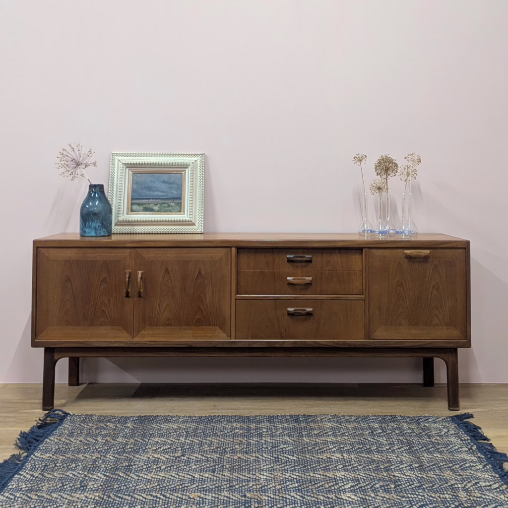 Designed by Donald Gomme as part of his 1960's Sierra range for G Plan, this is the much sought after, large teak sideboard. And it is large at over 2M in width! Expertly made in a mix of solid teak, teak veneer and afromosia on the base, the wood grain is striped in honey-toned bands, a beautiful characteristic of aged wood. It packs in a great deal of storage with a large, double door cupboard, three drawers at the top and a fall-door drinks cabinet. It's ideal for the dining room, lounge or family space where things need to be stowed regularly. Overall, the design is solid and substantial with chunky legs and sharp lines giving a boxy, blocky look. We love the recessed upper drawers. Make a serious midcentury style statement with a grand, 'hero' piece like this in your home.