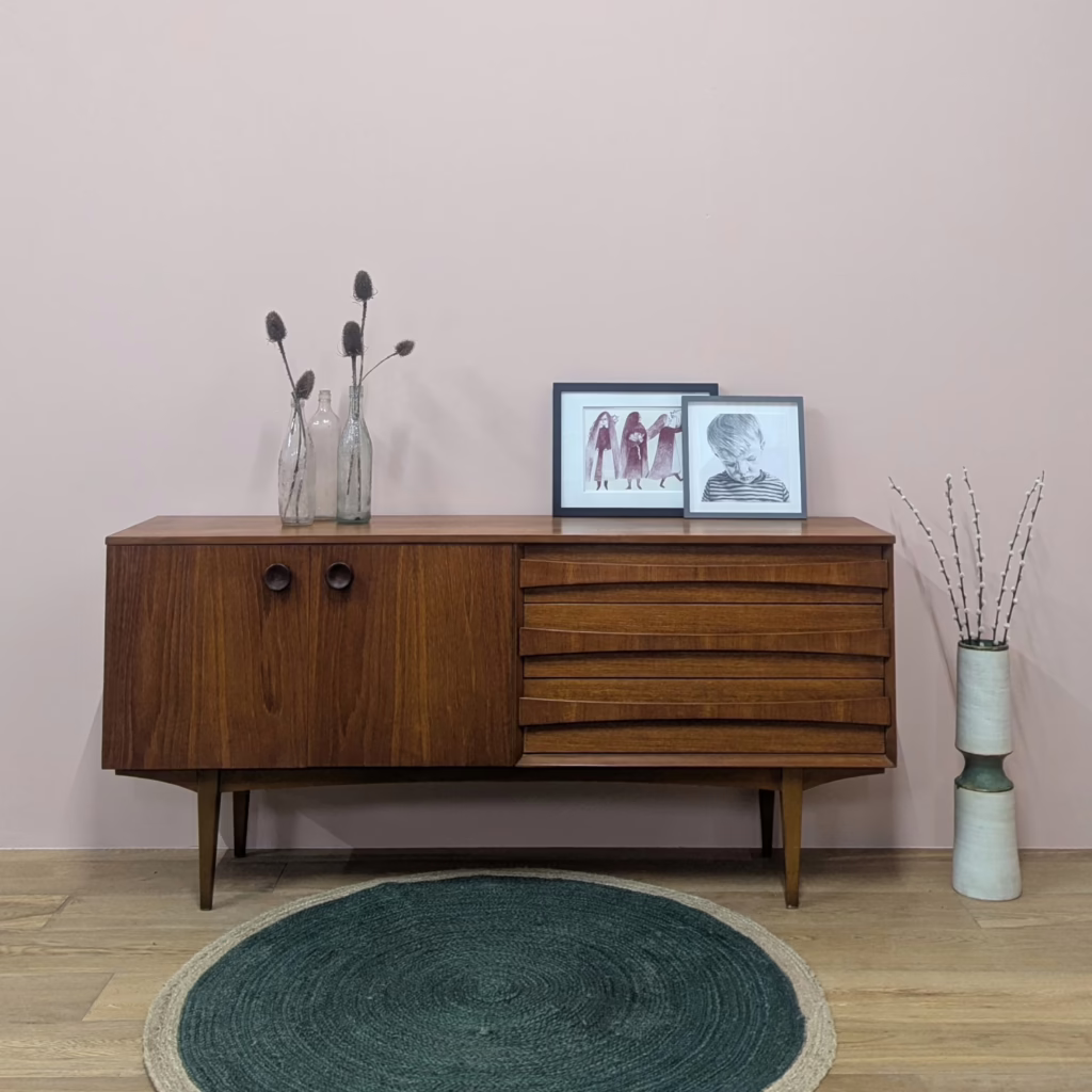 Something special from the British MCM era, this exceptionally handsome, 1960s sideboard by Lebus was clearly influenced by the Scandinavian design of the day, especially the curved handles on the drawers, so reminiscent of both Arne Vodder and Sven Anderson's designs. Made in teak, the overall look is pared back and minimal, accented with refined details like those drawer fronts and the slender, tapering legs which create space under and around this piece (plus you can hoover easily!). And we like the size of this particular piece. It's not an absolute beast as so many midcentury sideboards are. With a width of just over 1.6 metres and a shallow depth of 39cm, it's not too wall or space hungry but the storage capacity isn't compromised. There's plenty of room for stowing stuff away. Checked and serviced to last another 60+ years, it comes in superb condition.

&nbsp;